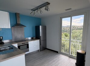 Eine moderne Küche mit einem Edelstahlkühlschrank, einem Einbauofen und einem Gasherd. Ein großes Fenster bietet Blick auf eine grüne Landschaft.