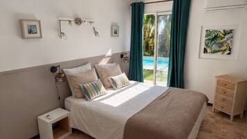 Une chambre à coucher comprenant un lit, des tables de chevet, une commode, une fenêtre avec des rideaux et une vue sur une piscine.