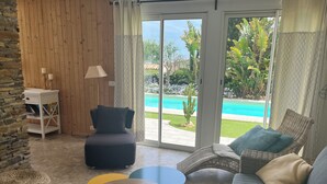 Un salon moderne avec vue sur la piscine, un canapé en osier, une petite table et une bibliothèque.