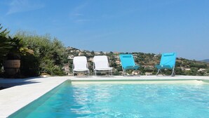 Une piscine d’un bleu éclatant, dotée de chaises longues et offrant une vue sur une colline en arrière-plan.