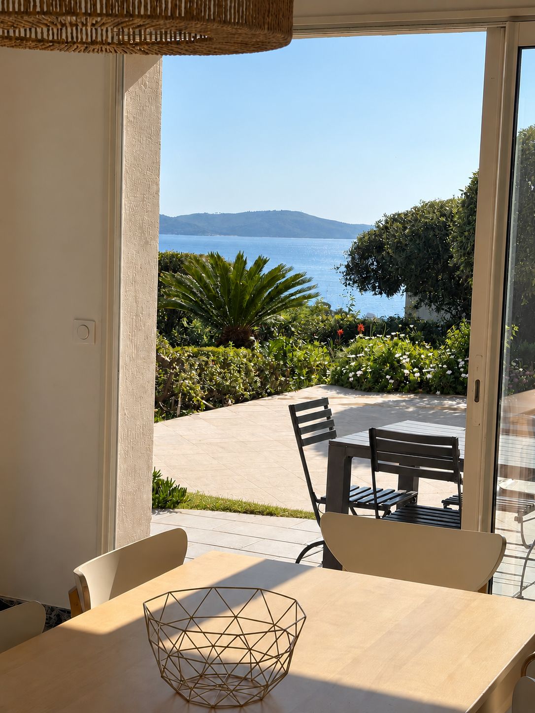 A dining area with a table and chairs, a woven ceiling, and a view of the sea and hills.