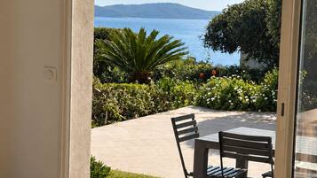 A dining area with a table and chairs, a woven ceiling, and a view of the sea and hills.
