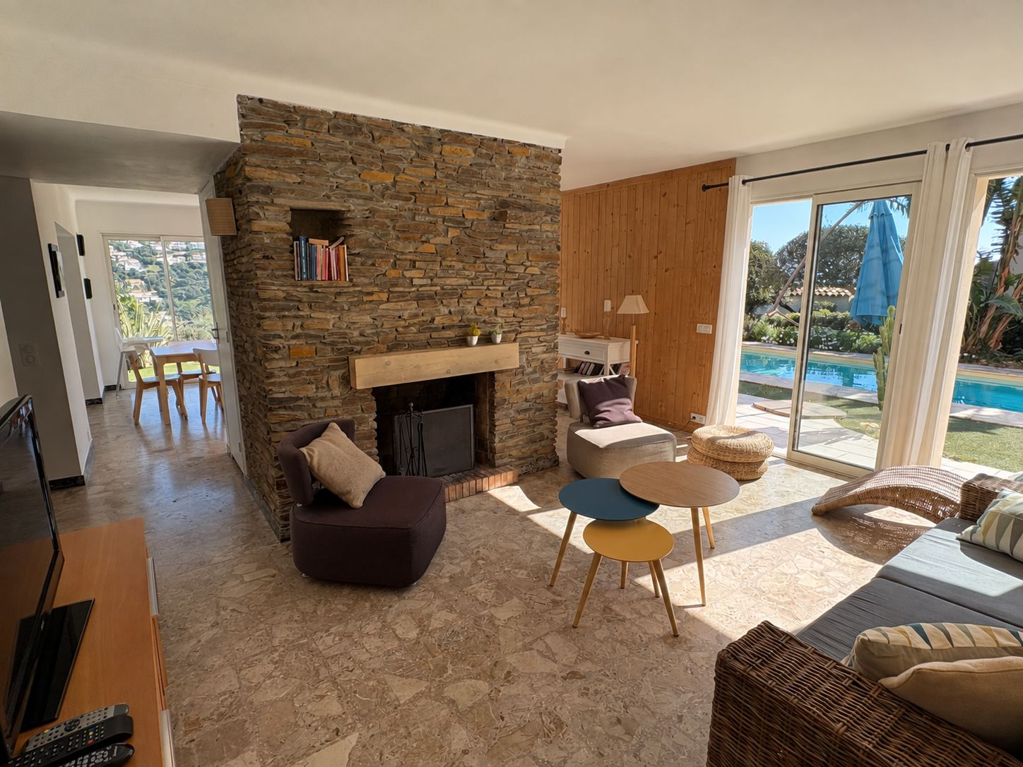 A living room with a stone wall, a fireplace, a pool view, and a dining area.
