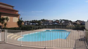 A swimming pool with a white fence, surrounded by a residential area with houses and palm trees. - Apartment for 6 persons with swimming-pool and tennis in condominium (Capbreton)