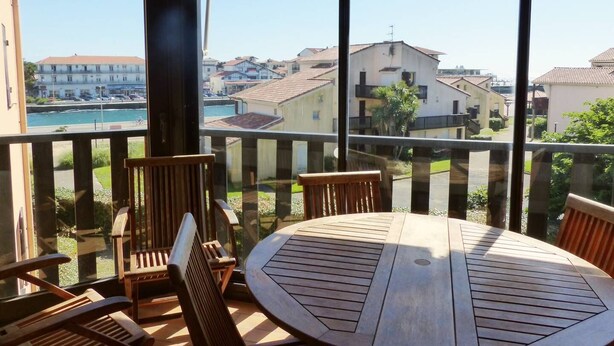 A balcony with a wooden table and chairs, overlooking a residential area with houses and a body of water. - Apartment for 6 persons with swimming-pool and tennis in condominium (Capbreton)