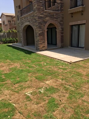 Un edificio residencial con fachada de piedra, un balcón con barandilla negra y un patio pavimentado.