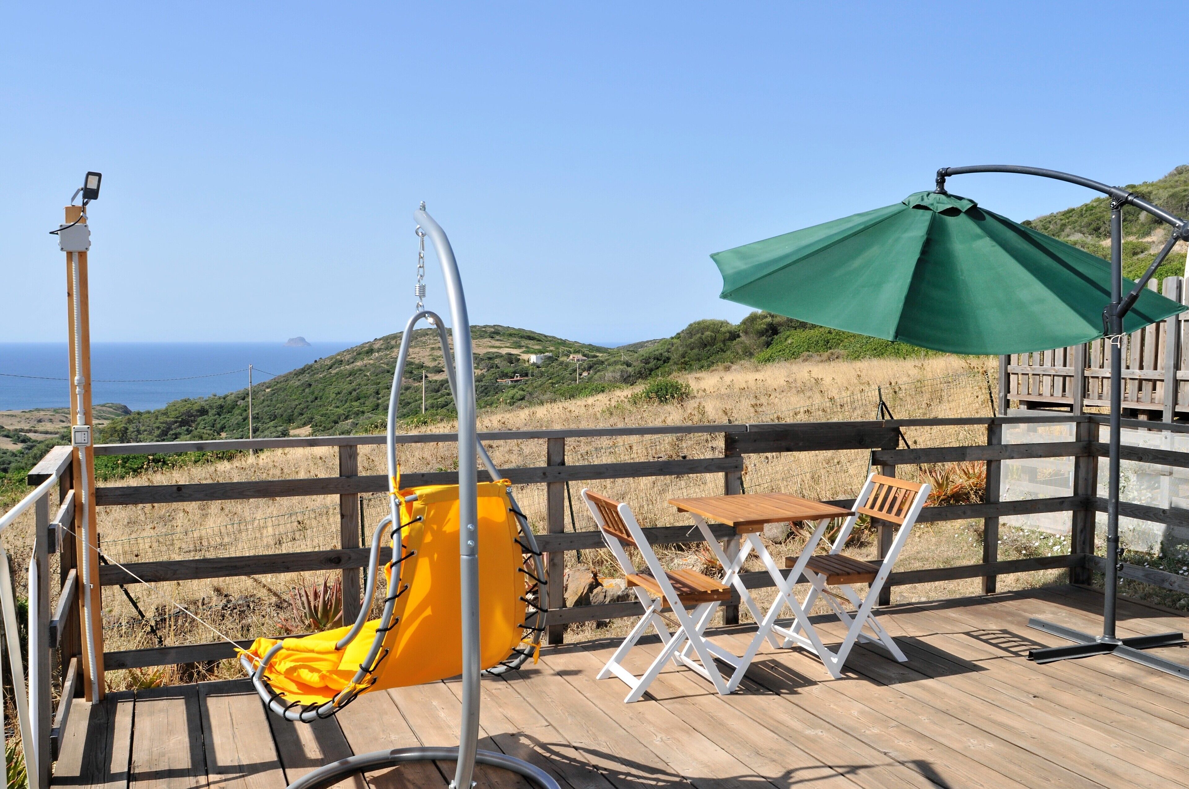 Une terrasse en bois avec une chaise suspendue, une table et un parasol.