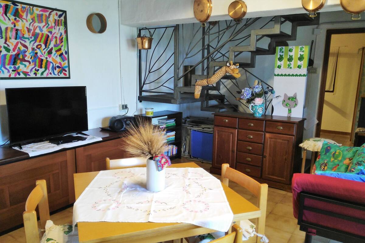 Ein gemütliches Wohnzimmer mit Fernseher, einem Esstisch mit Stühlen, einer Küchenzeile und einer Giraffendekoration sowie einer Treppe.