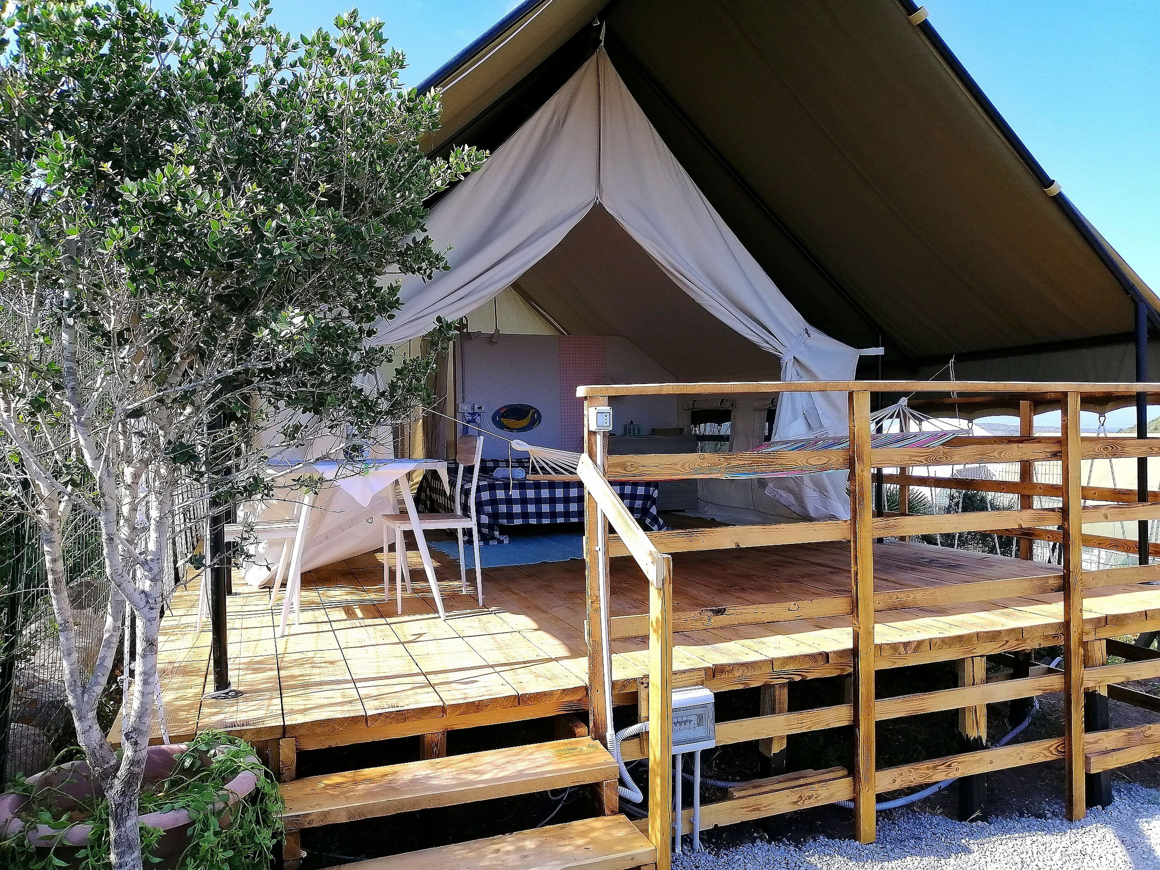 Une terrasse en bois avec une structure en forme de tente, un lit et une table.