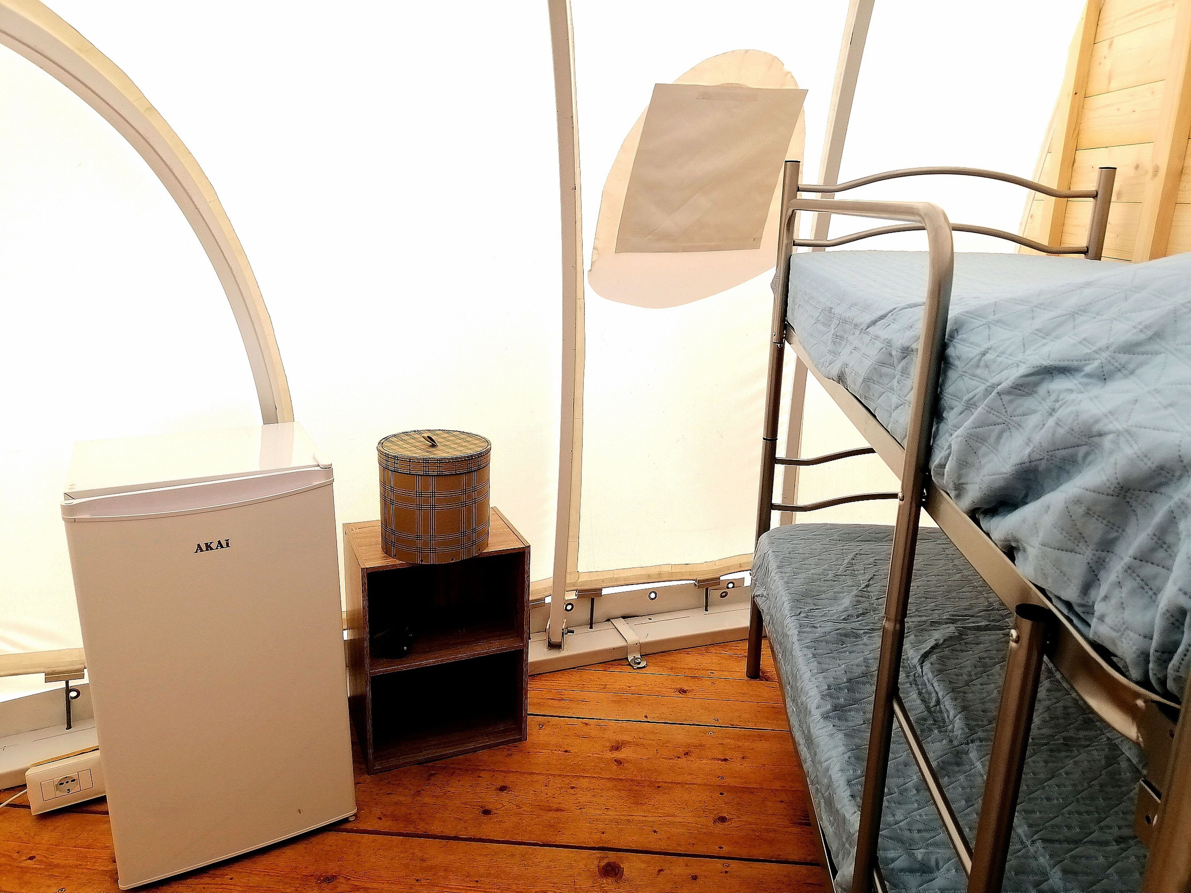 Ein Etagenbett mit Matratze, ein kleiner, weißer Kühlschrank und ein Holzschrank mit einem Behälter in Karomuster.