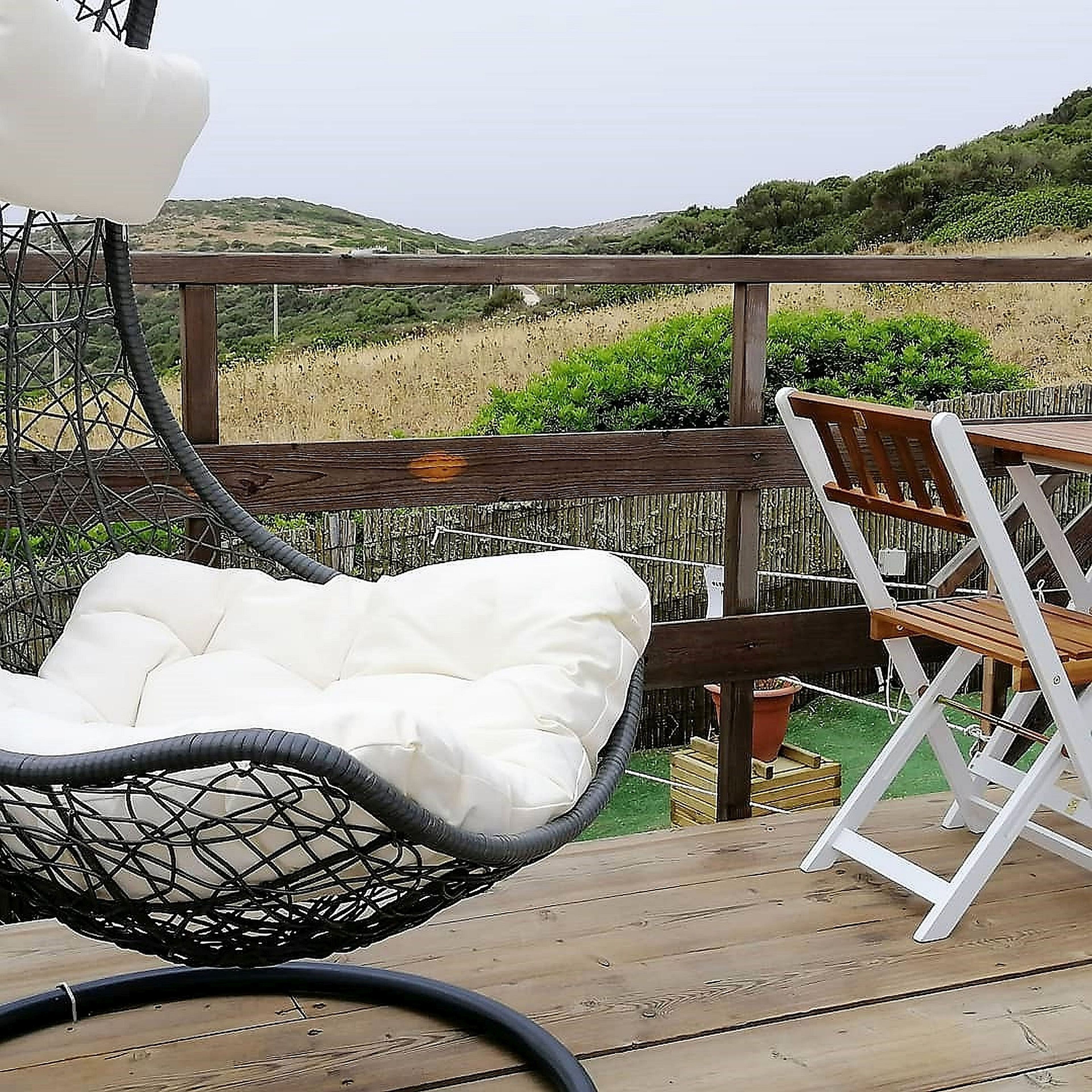 Una terraza de madera con una silla blanca acolchada y una mesa de madera.