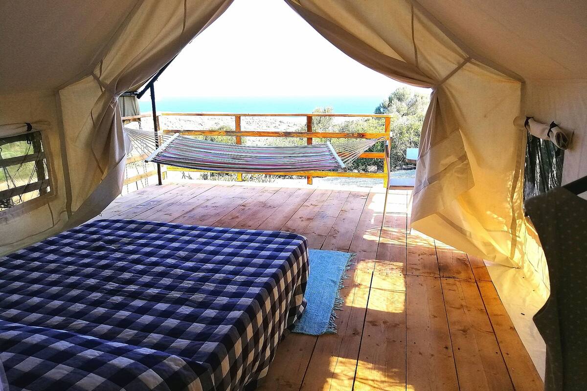 Eine Zelteinrichtung mit Bett, Hängematte und Meerblick.