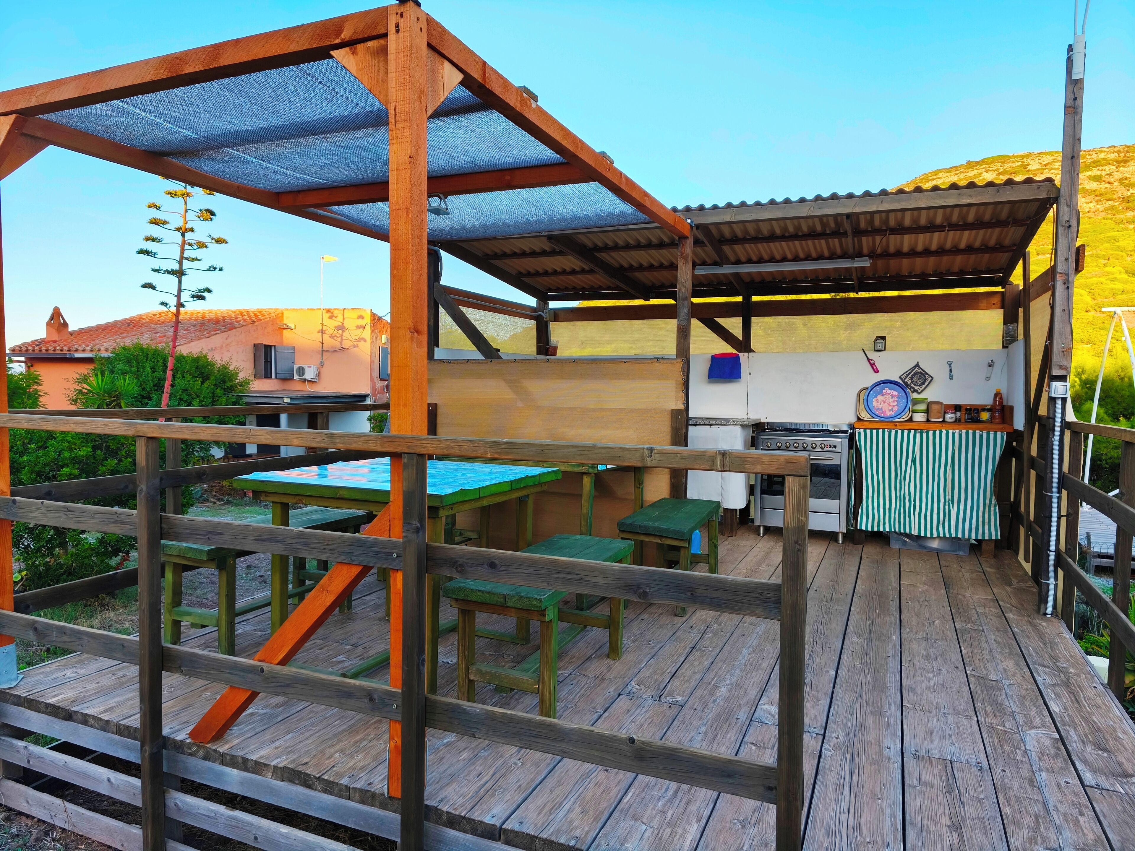 A rustic outdoor kitchen area with wooden tables and benches, a gas stove, and a sink.