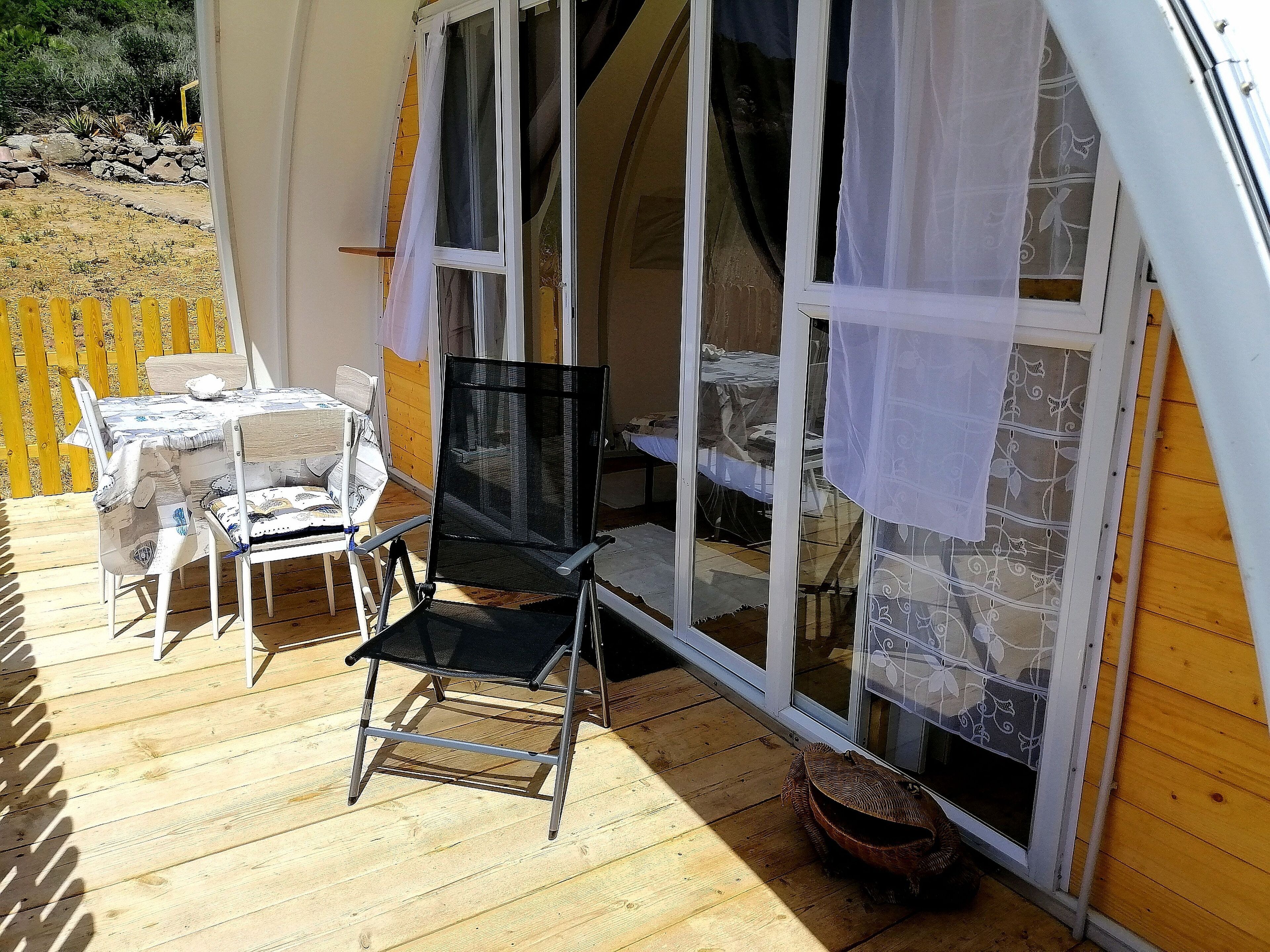 Une terrasse en bois avec une table et des chaises, une chaise noire et un panier en osier.