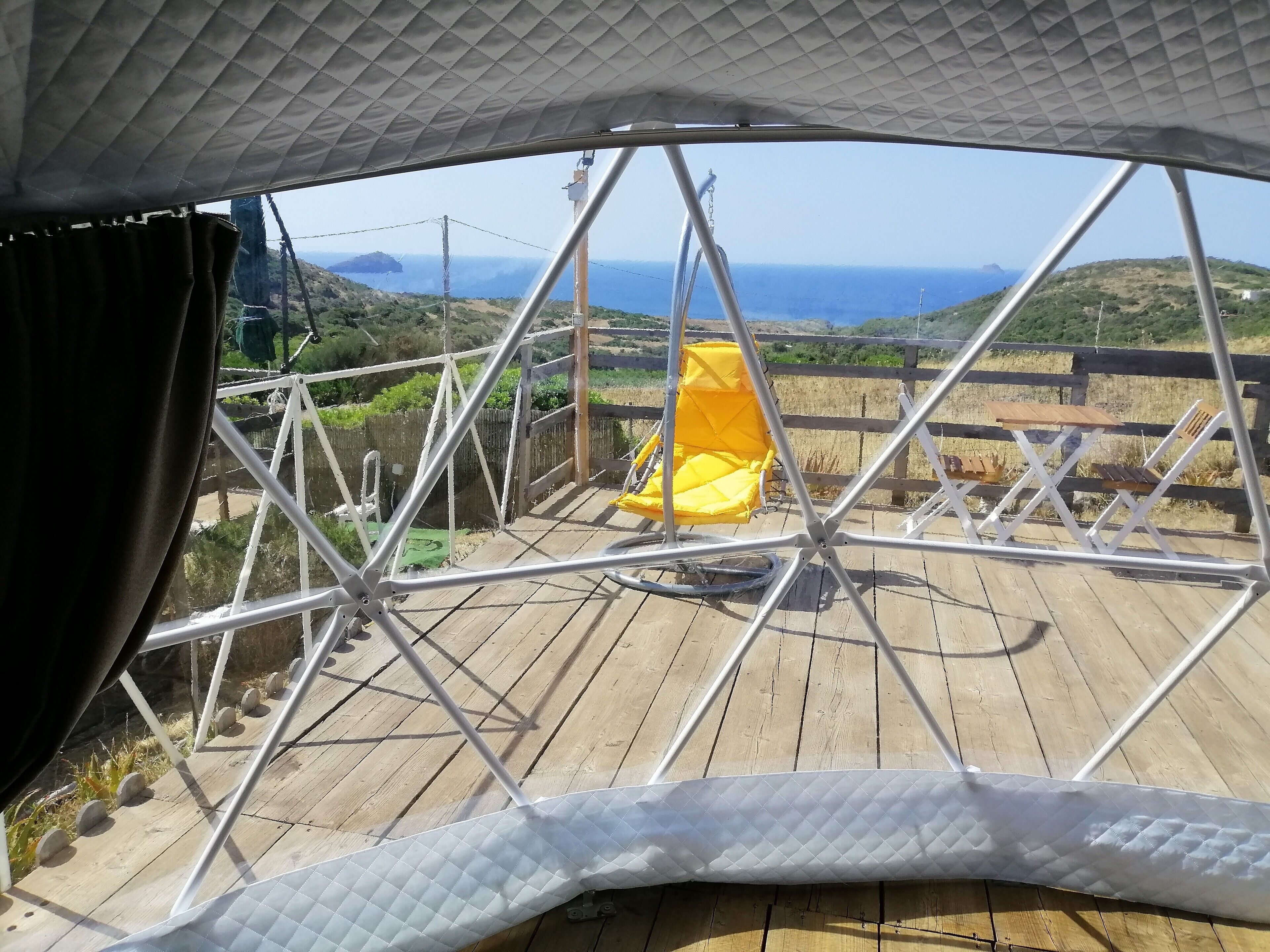 A covered outdoor seating area with a view of the sea and hills.