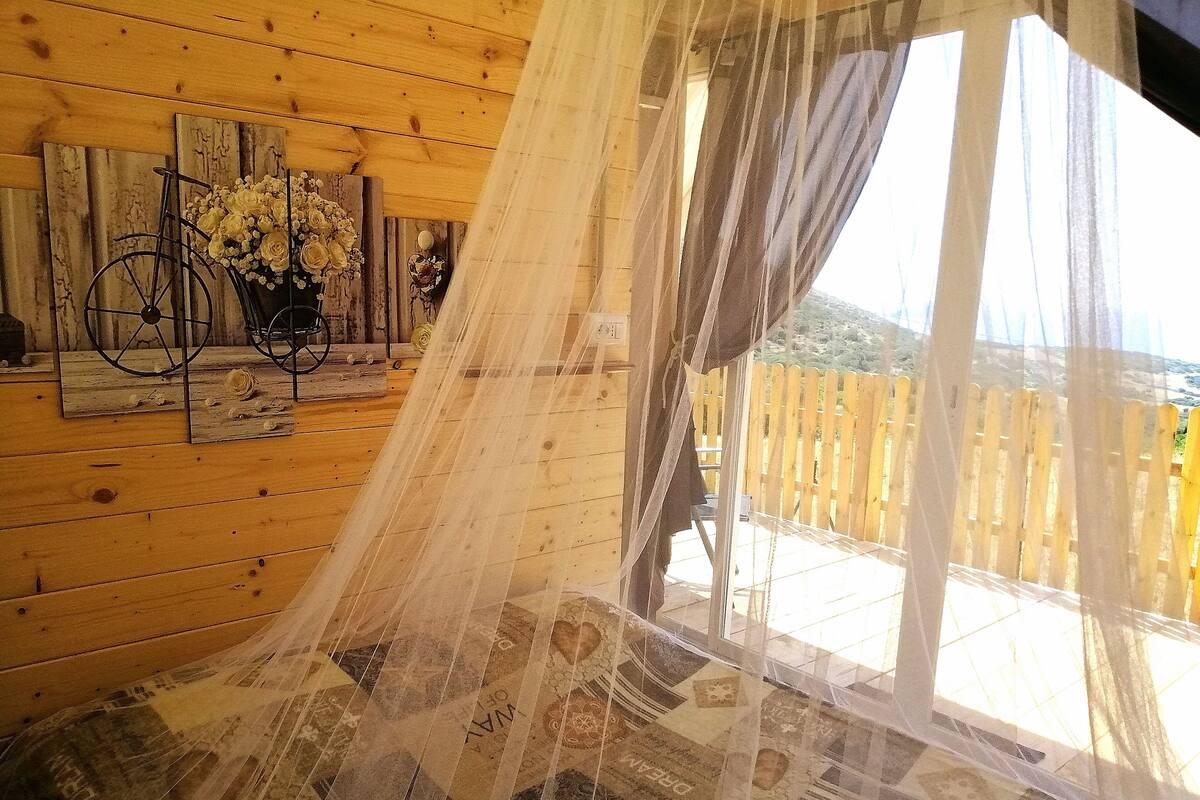 Ein Zimmer mit Holzwänden, einem großen Fenster mit leichtem Vorhang, einem Fahrrad und einem an der Wand befestigten Kunstwerk.