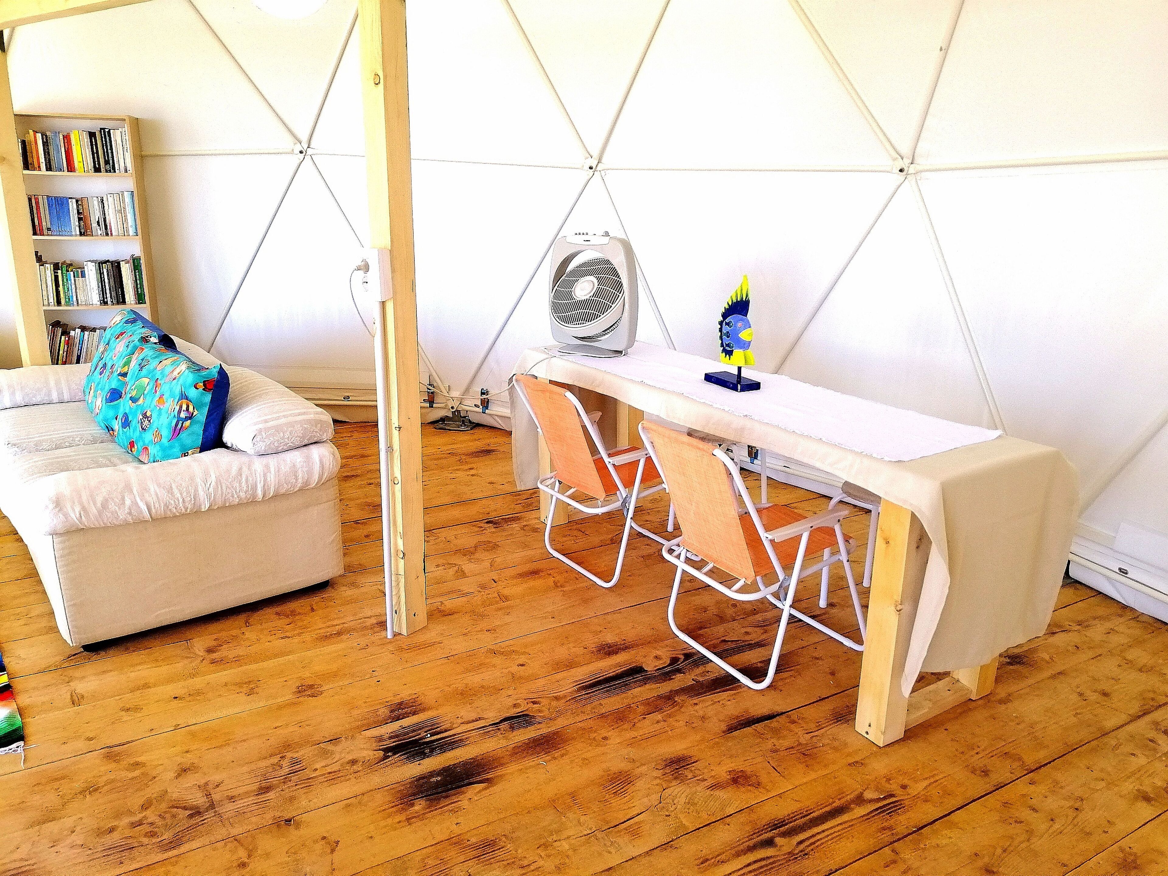 Une pièce avec un canapé blanc, une petite table, un ventilateur et une bibliothèque.