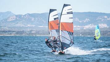 Una persona practica windsurf en un lago con montañas al fondo.