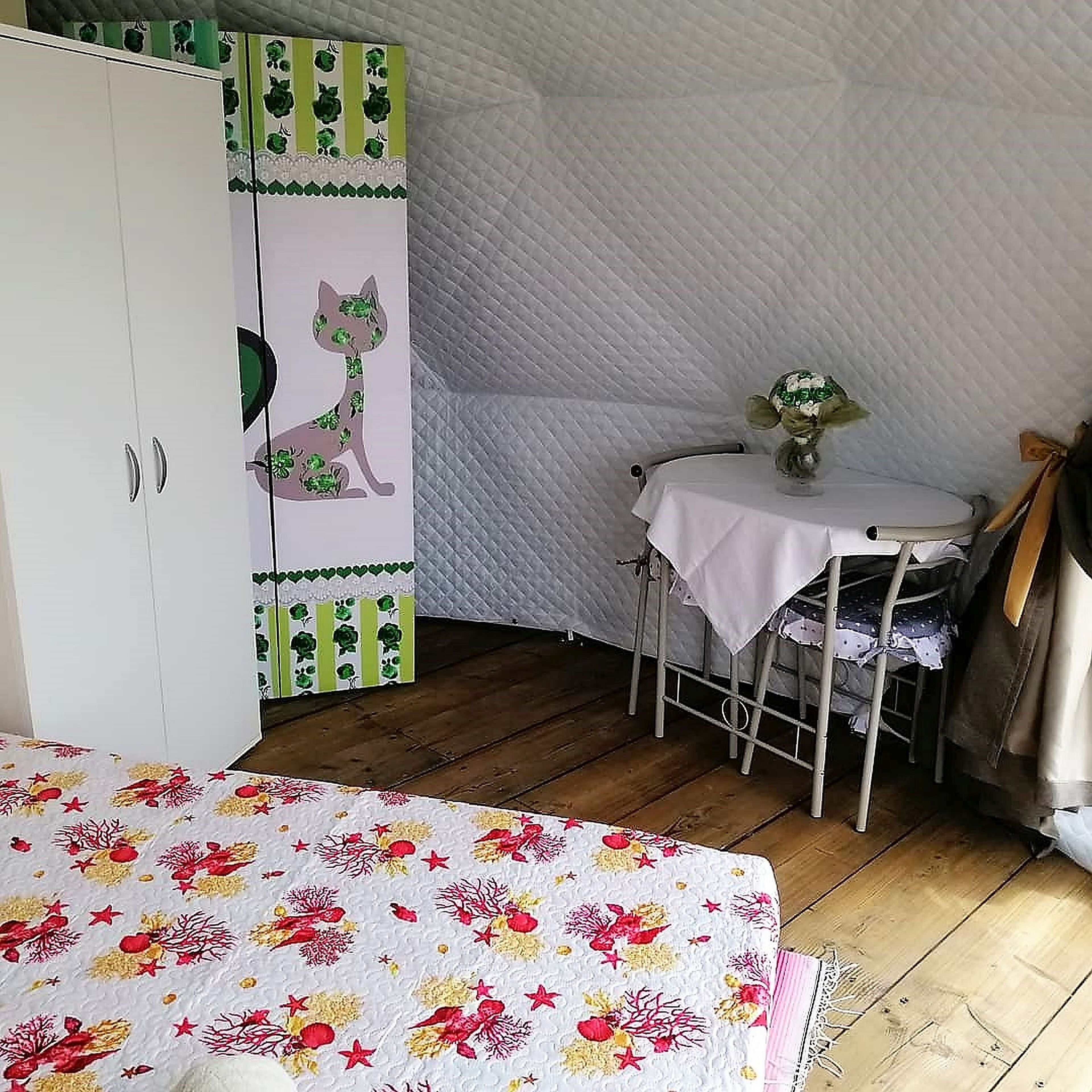 A bedroom with a bed, a wardrobe, a small table with a vase, and a chair.