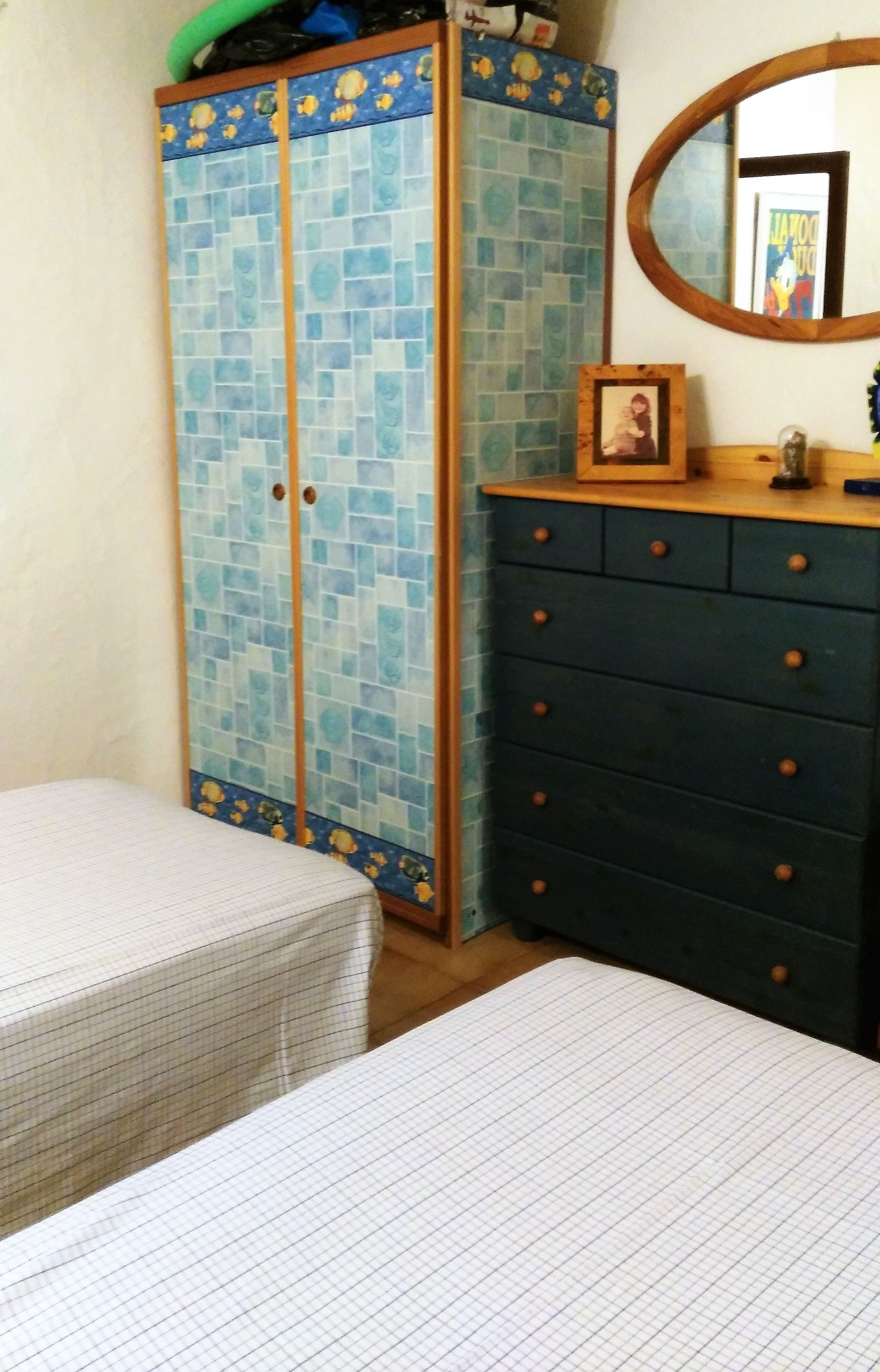 A bedroom with two beds, a wardrobe with a tiled design, a dresser with drawers, and a mirror on the wall.
