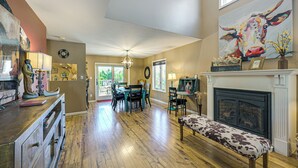 A spacious living room with hardwood floors, a fireplace, a dining area with chairs, and a large painting on the wall.