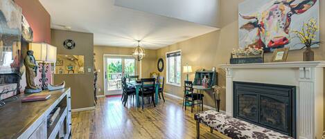 A spacious living room with hardwood floors, a fireplace, a dining area with chairs, and a large painting on the wall.