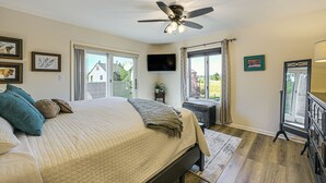 A bedroom with a bed, ceiling fan, TV, and a view of the outside.