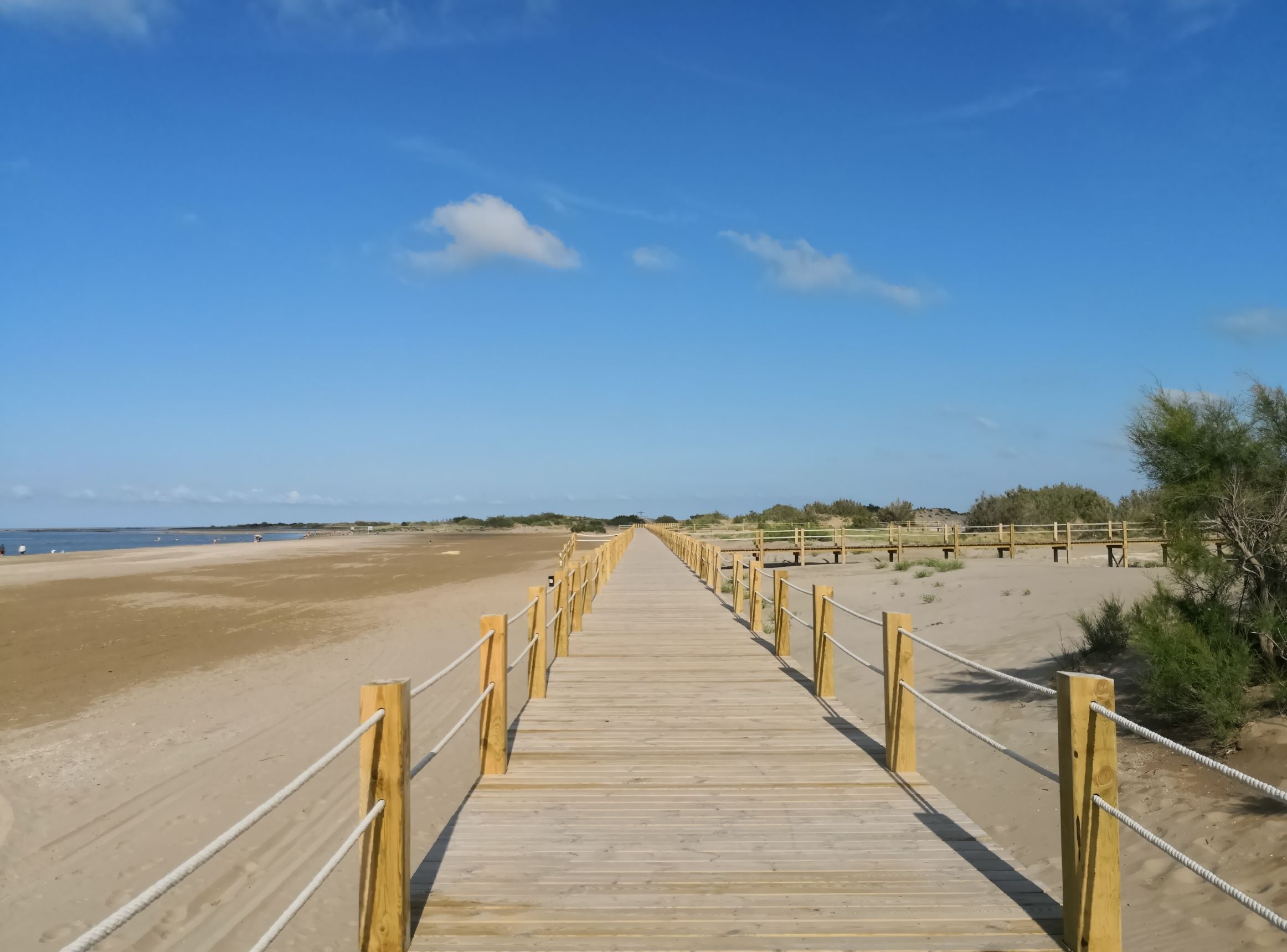 A wooden boardwalk leading to a beach with a clear sky.