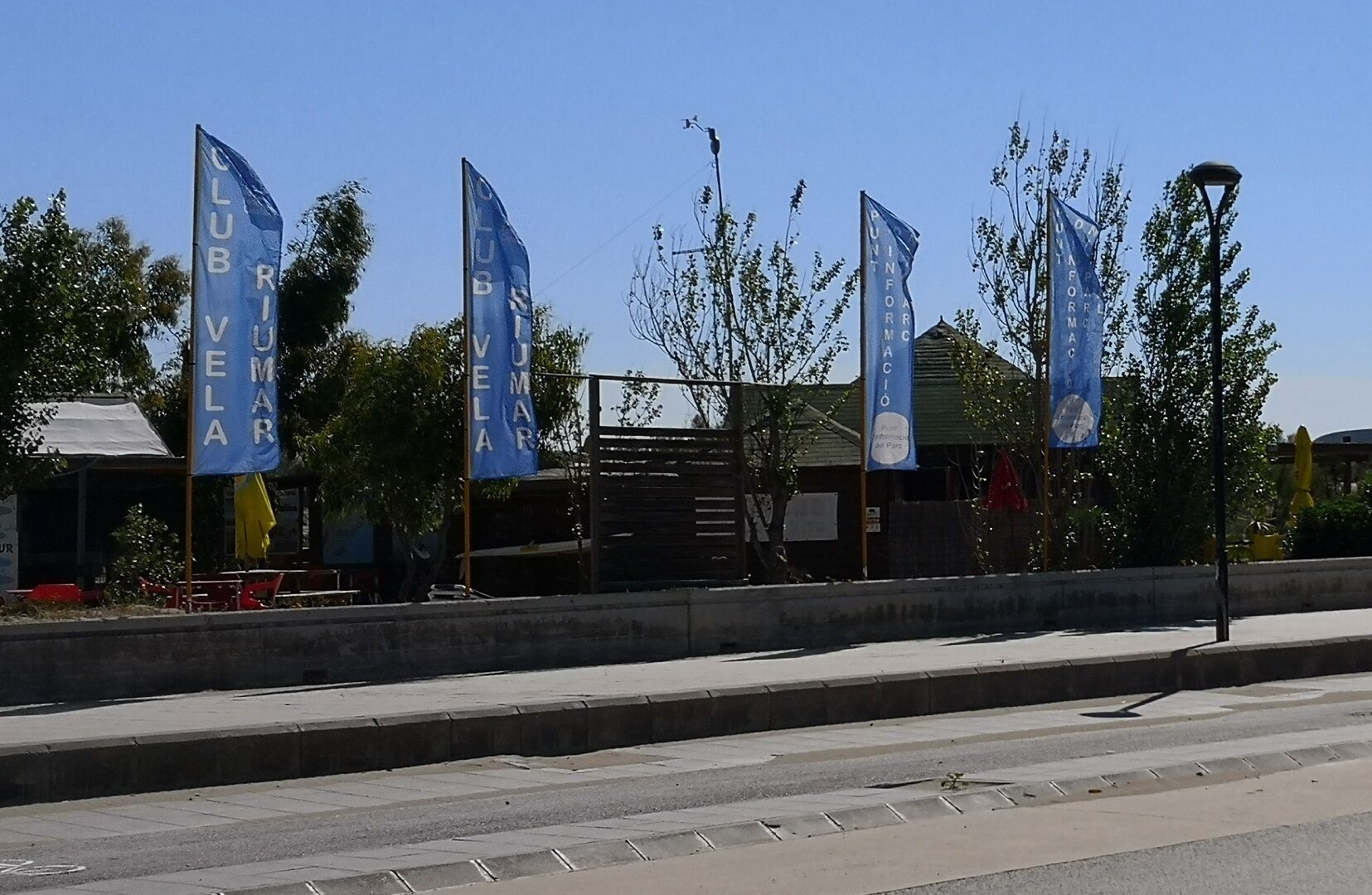 A street with multiple blue flags, a sidewalk, and a building with a green roof.