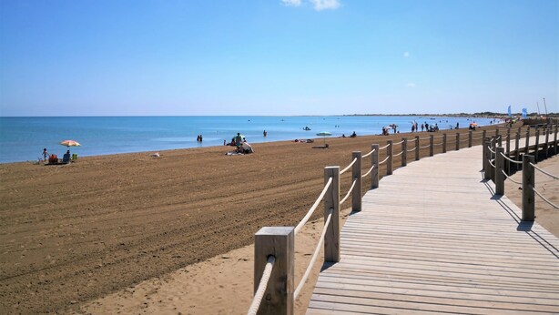 Una passerella di legno che conduce a una spiaggia sabbiosa con acque blu cristalline.