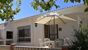 Un patio con tavolo e sedie, un tubo da giardino sospeso e un ombrellone bianco.