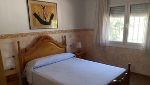 Una camera da letto con un letto in legno, un comodino, una lampada, una finestra con persiane e un quadro appeso al muro.