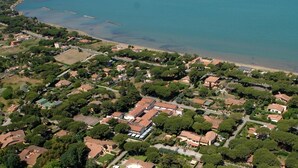 An aerial view of a coastal residential area with houses, a beach, and a large building with a red roof.