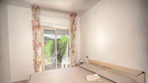A bedroom with a bed, an open book, a chair, and a view of greenery outside.