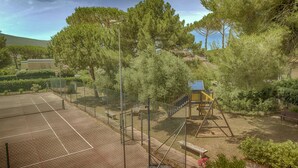 A tennis court surrounded by trees and a playground.