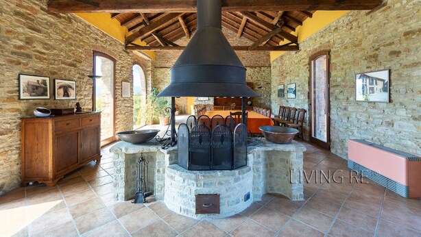 Une pièce rustique aux murs de pierre, dotée d’une grande cheminée en pierre, de poutres en bois au plafond et d’un coin repas avec une table et des chaises.
