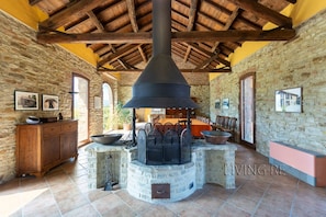 A rustic stone-walled room with a large stone fireplace, wooden beams on the ceiling, and a dining area with a table and chairs.