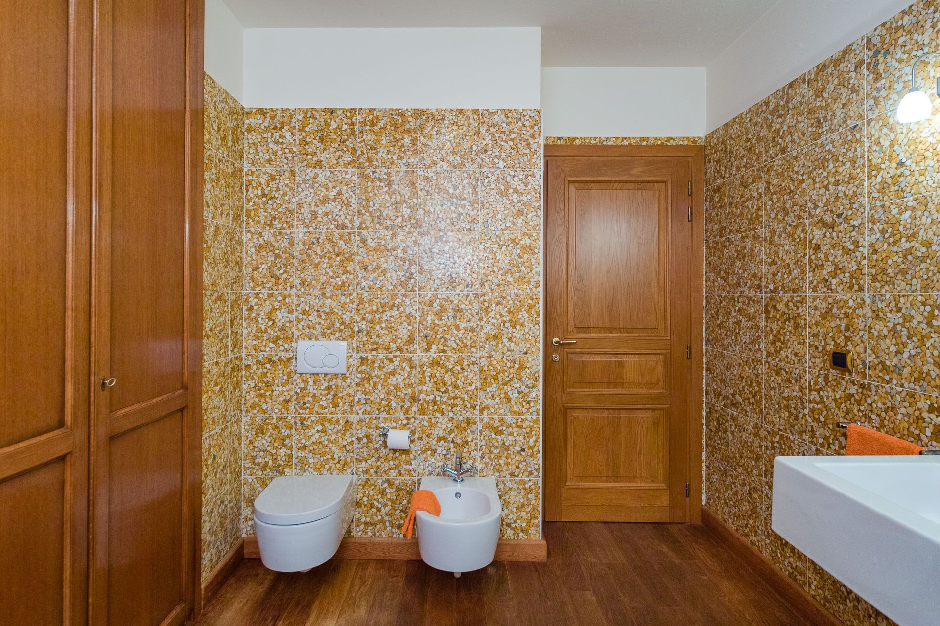 A bathroom with a toilet, bidet, and sink, all with wooden cabinets.
