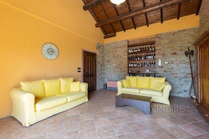 A living room with two yellow sofas, a tiled floor, a stone wall, and a wine rack.