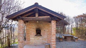 Une construction rustique en briques, avec un toit en bois, une cheminée et un banc en pierre.