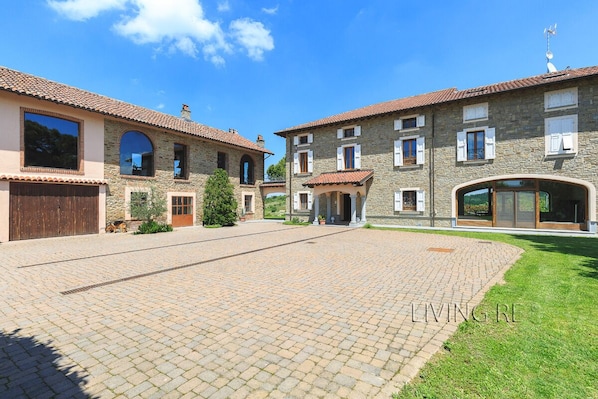 A courtyard with a paved area, stone buildings with arched windows, and a grassy lawn.