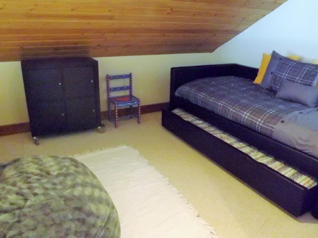 Een slaapkamer met een hoogslaper, een kleine stoel, een kast en een rond poef.