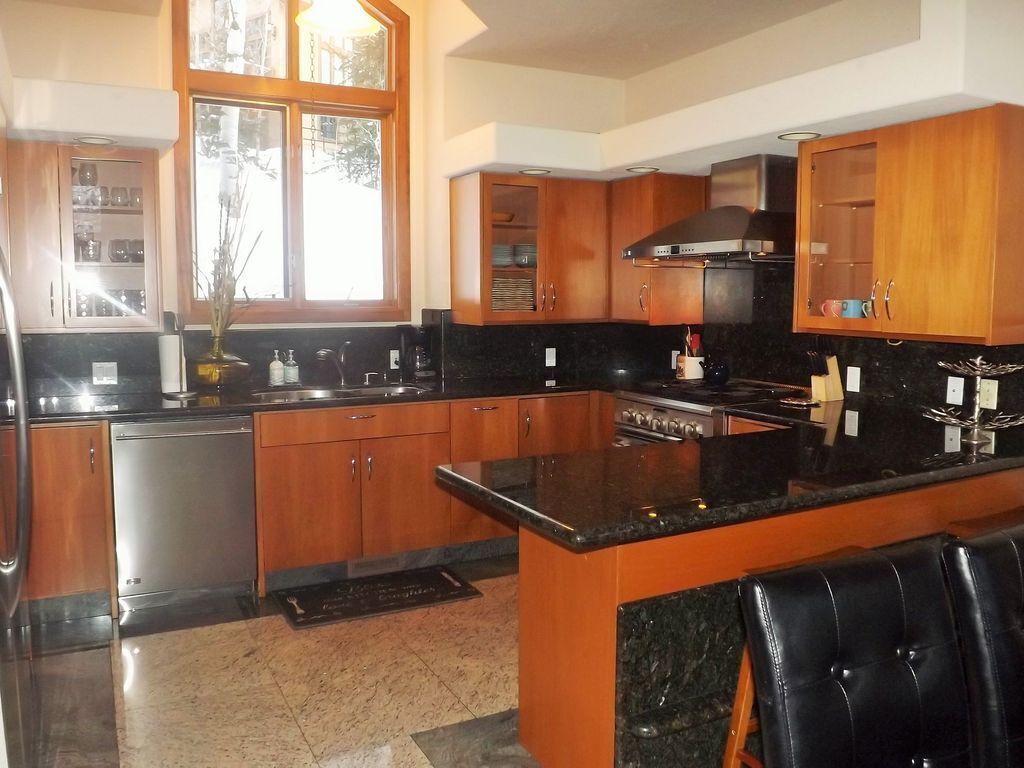 A kitchen with wooden cabinets, a black countertop, stainless steel appliances, and a window with a view.