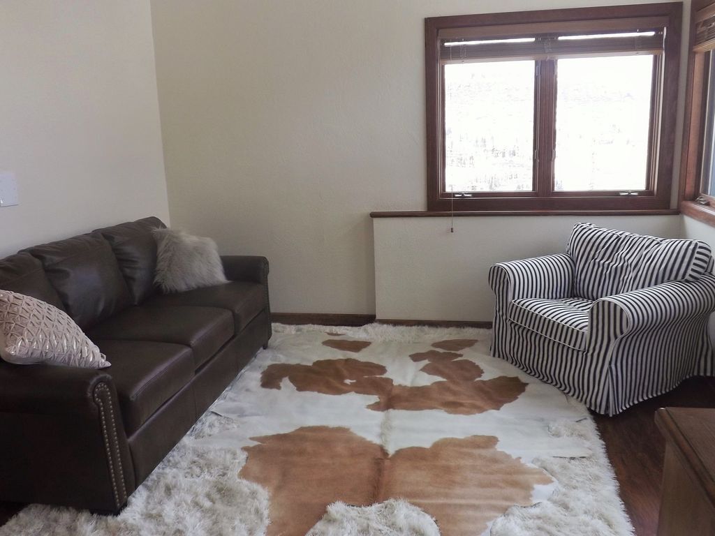 Una sala de estar con un sofá de cuero marrón, un sillón a rayas y un tapete de piel de vaca.