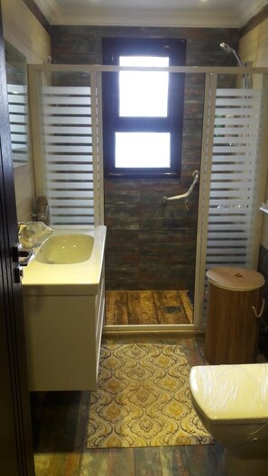 Een badkamer met een douchecabine van glas, een wastafel en een toilet.