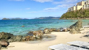 Una platja amb aigua turquesa cristal·lina, un litoral rocos i un edifici de resort al fons.
