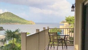 Un balcó amb vista al mar, una taula amb caires i una jardiniera amb plantes tropicals.