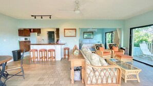 Zona d'estar àmplia amb sofà, cadires, taula de dinar i cuina al fons.
