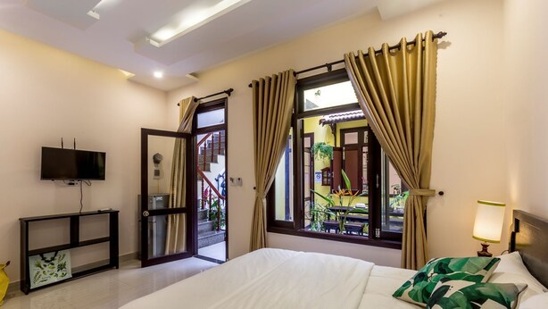 Quarto de hotel com cama, televisão, escrivaninha e janela com cortinas.