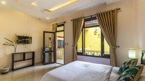 Quarto com cama, televisão, mesa de apoio e vista para a varanda.